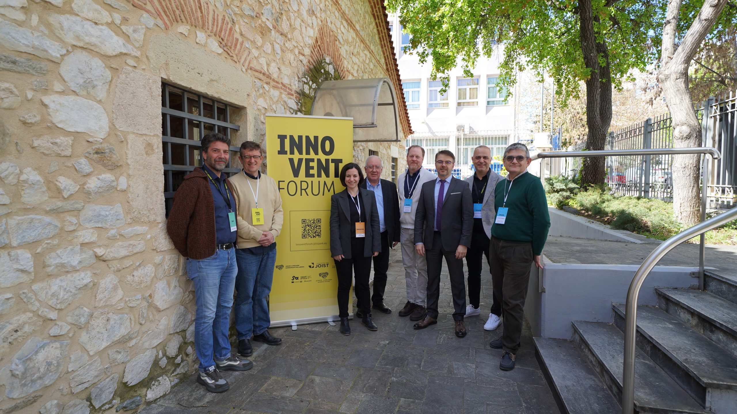 participants gathered outside the venue next to an Innovent Forum banner during the AI-SECRETT workshop in Larissa